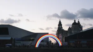 A glowing rainbow arch installation located in front of Liverpool's historic waterfront buildings.