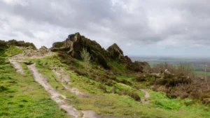 A rural grassy hillside path and rock formations under a cloudy UK sky.