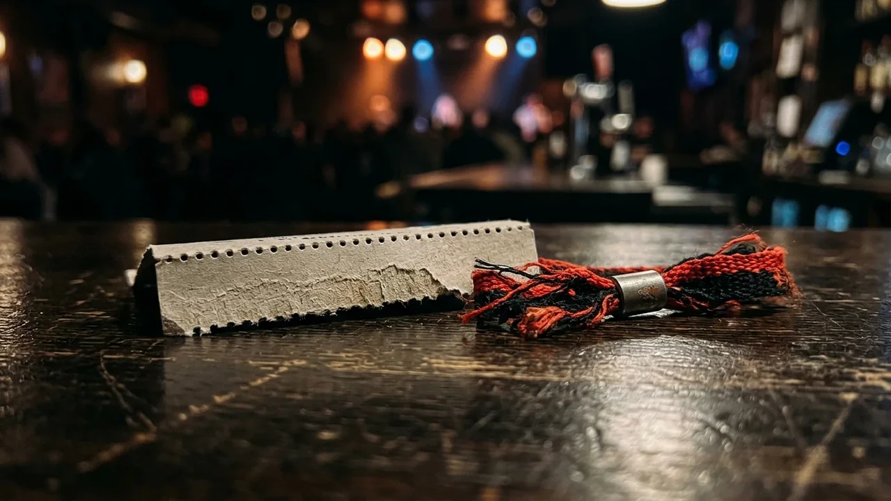 A concert ticket stub and fabric wristband resting on a dark wooden bar counter.
