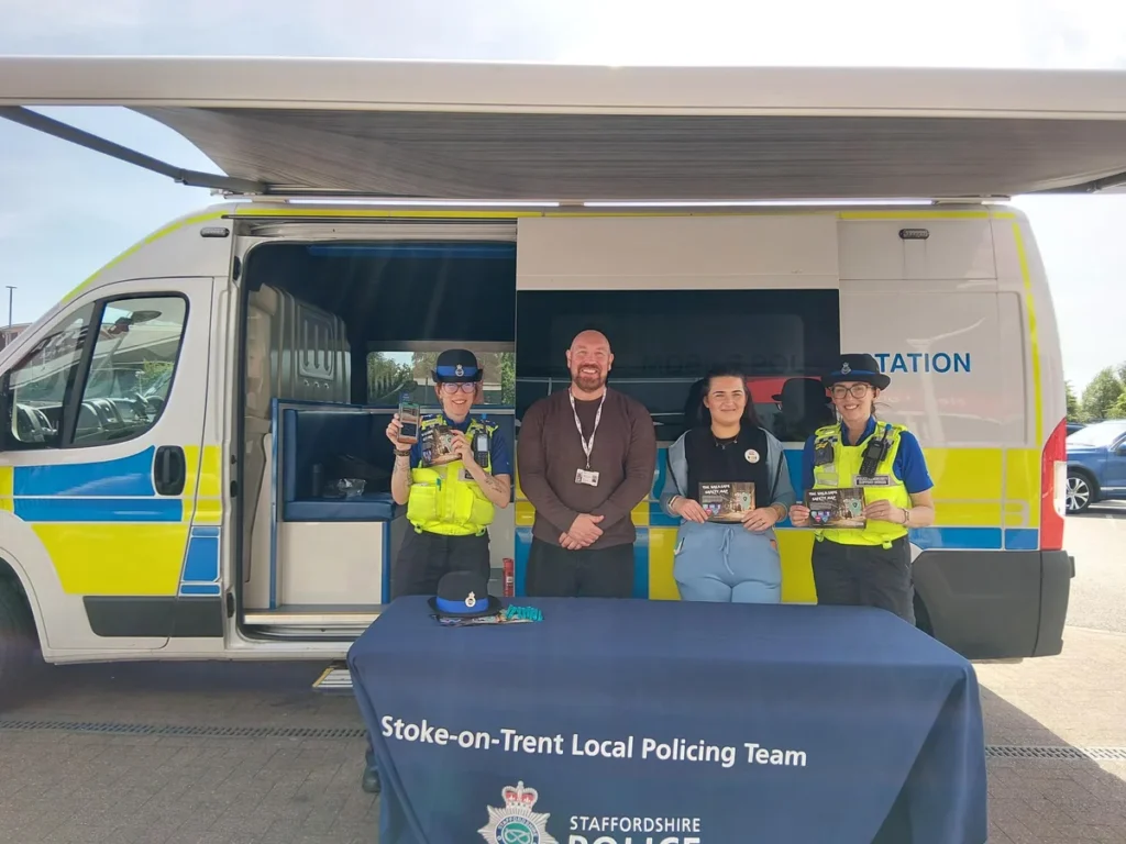 Two police officers and two civilians stand before a mobile police station van.