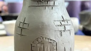 A close-up of a clay pottery piece featuring hand-carved brick and window patterns.