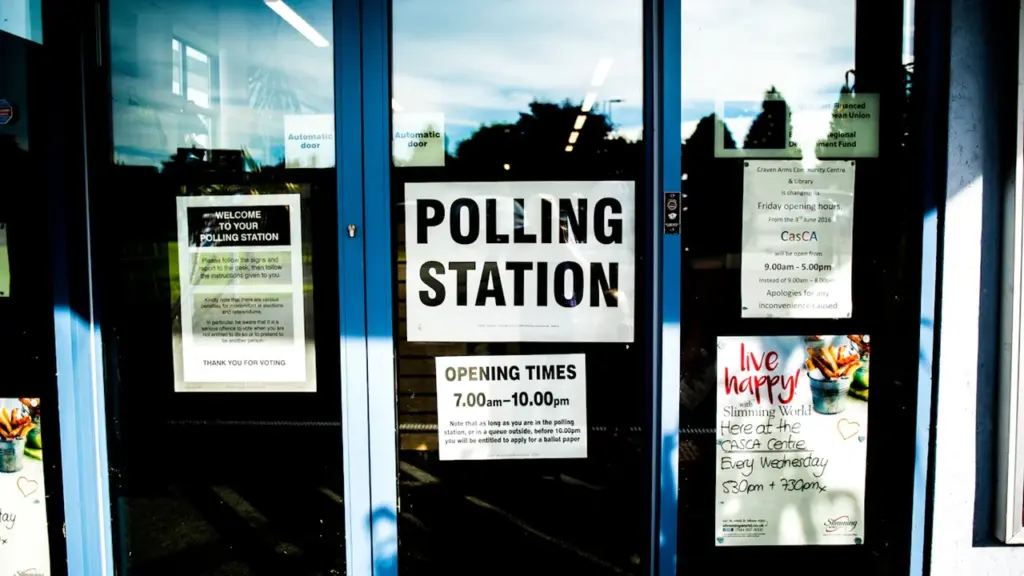A clear glass door at a polling station with informational posters displayed inside.