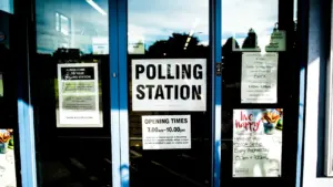 A clear glass door at a polling station with informational posters displayed inside.