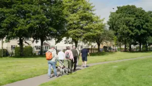 Group of people walking their dogs along a sunlit park path in England