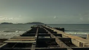 An old concrete pier extending into the calm sea, symbolizing industrial maritime development.