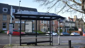 An empty modern glass and metal bus shelter situated on a paved sidewalk.