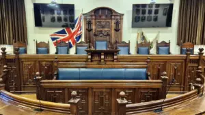 An empty formal courtroom featuring dark wooden benches, leather seats, and the British flag.