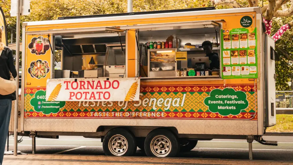 A brightly colored food truck parked on a street serving tornado potatoes and food.