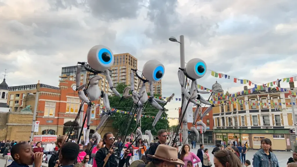 Large eye-shaped puppets performing in a public square in an English town.