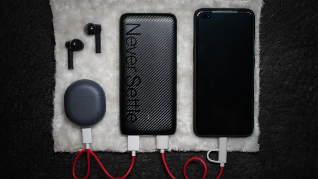 A power bank, smartphone, and earbuds connected by cables on a flat surface.