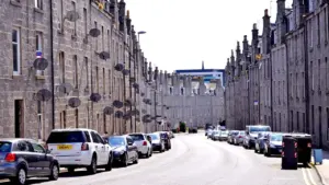 Street view of traditional grey granite tenements in Aberdeen, Scotland, with parked cars.