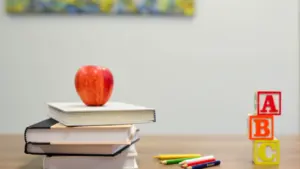 Red apple on stack of school books with educational wooden blocks on desk.
