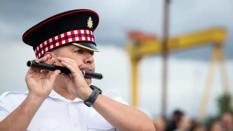 A man in a traditional police band uniform playing a black flute outdoors.