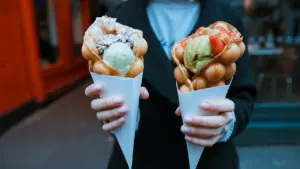 Person holding two bubble waffle ice cream cones at a street food festival.