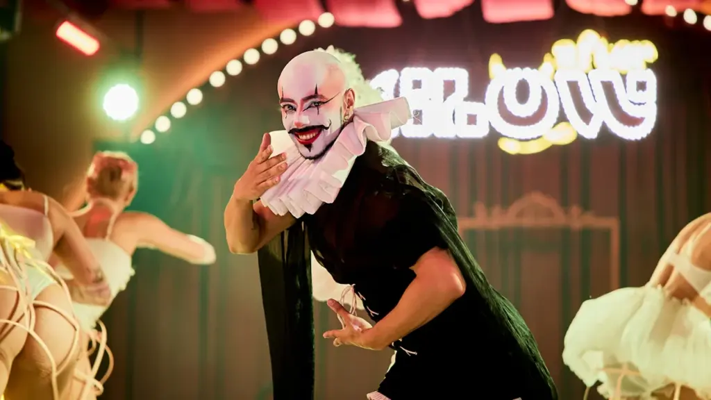 A performer in elaborate burlesque costume dancing on a vibrant, theatrical stage.