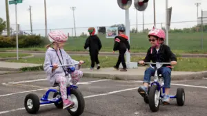 Children wearing helmets practicing road safety skills on a simulated outdoor cycling course.