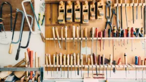 Organized collection of hand tools hanging on a wooden workshop wall rack.