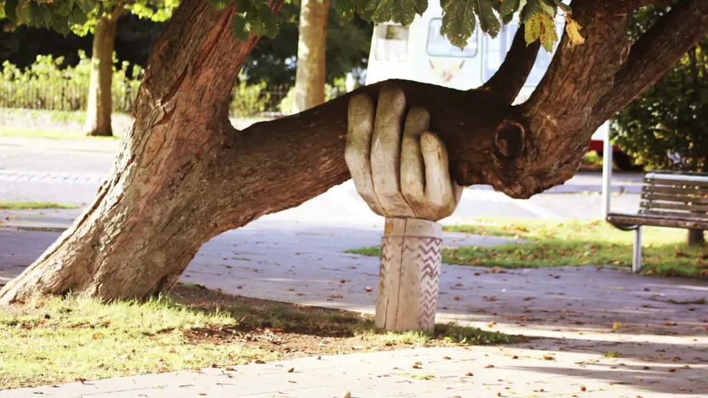 A public art sculpture of a hand supporting a tree branch in a park.