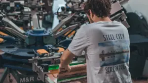 A man operates industrial screen printing machinery at a factory workstation in a studio.