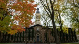 Classic brick university building with a clock tower surrounded by autumn trees.
