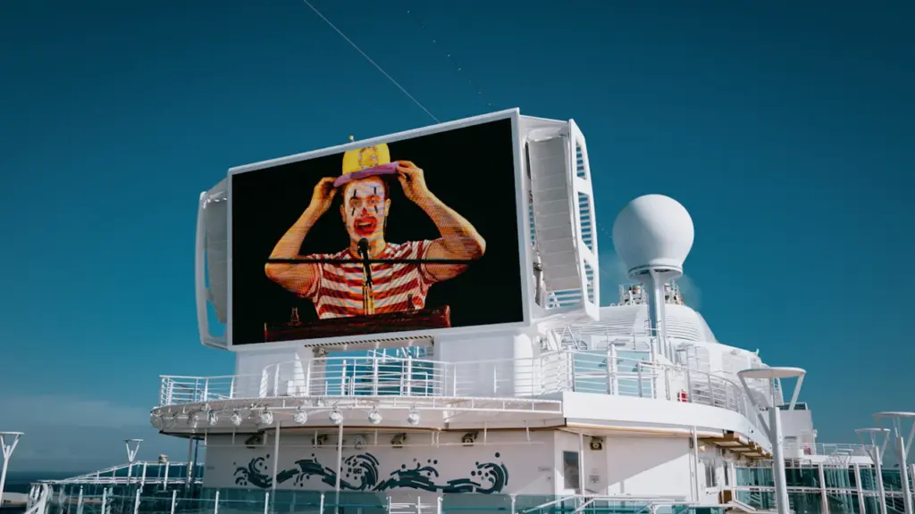 A large digital screen on a cruise ship deck displaying a circus performer.