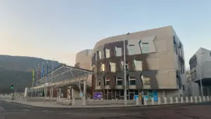 The modern architecture of the Scottish Parliament building with flags displayed outside under sky.