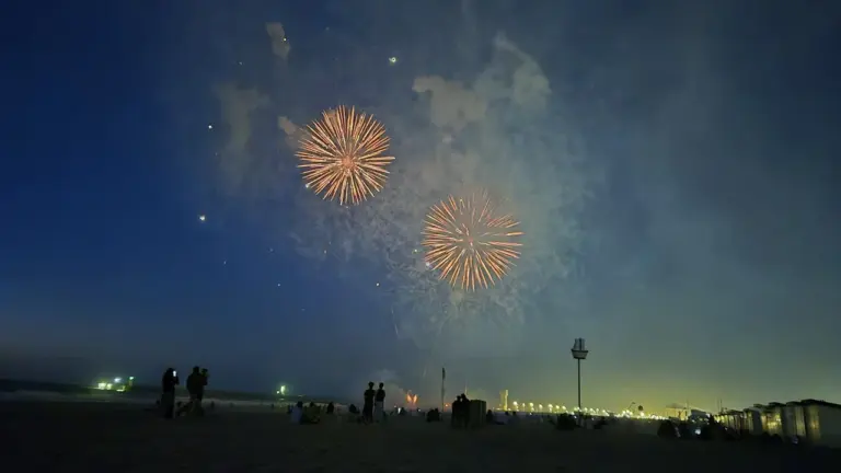 Spectacular fireworks illuminate the night sky over a sandy coastal beach at night.