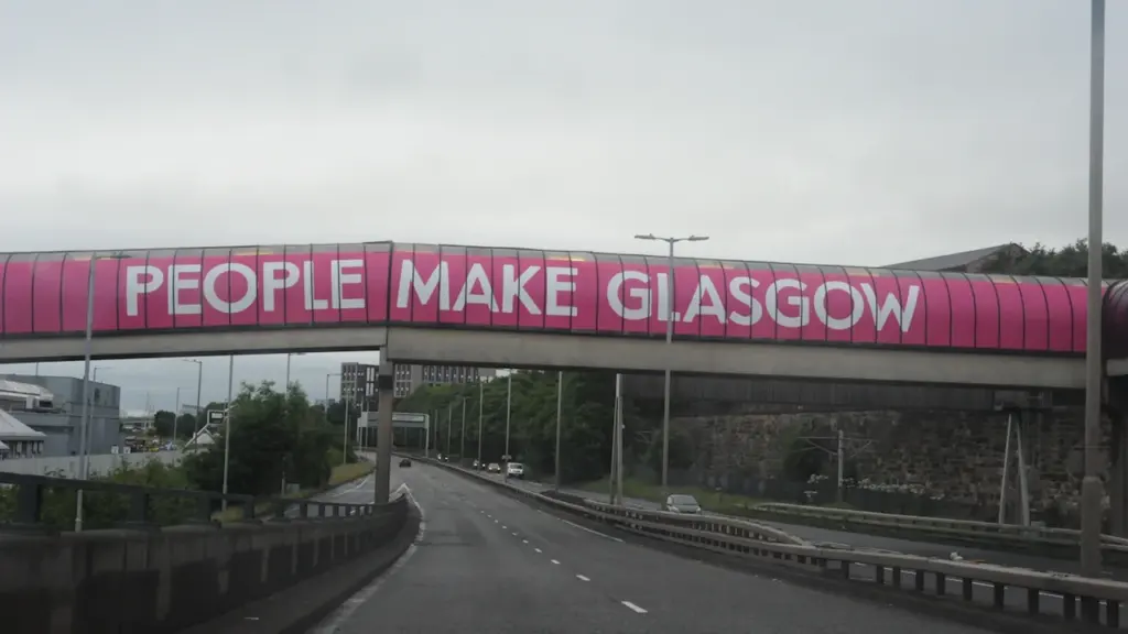 An overhead pedestrian bridge over a motorway featuring the famous People Make Glasgow branding.