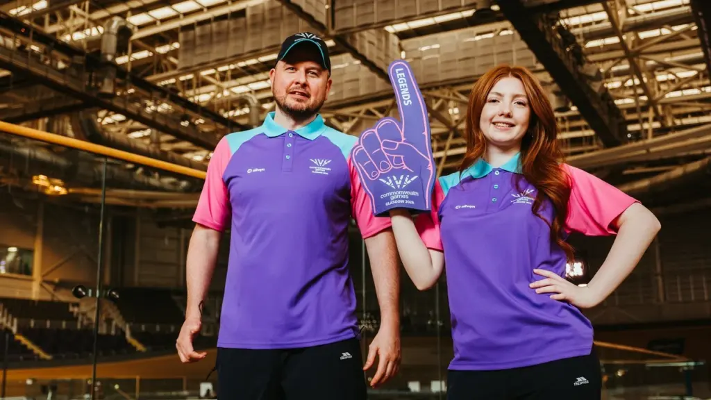 A man and a woman in purple staff uniforms posing inside a stadium.