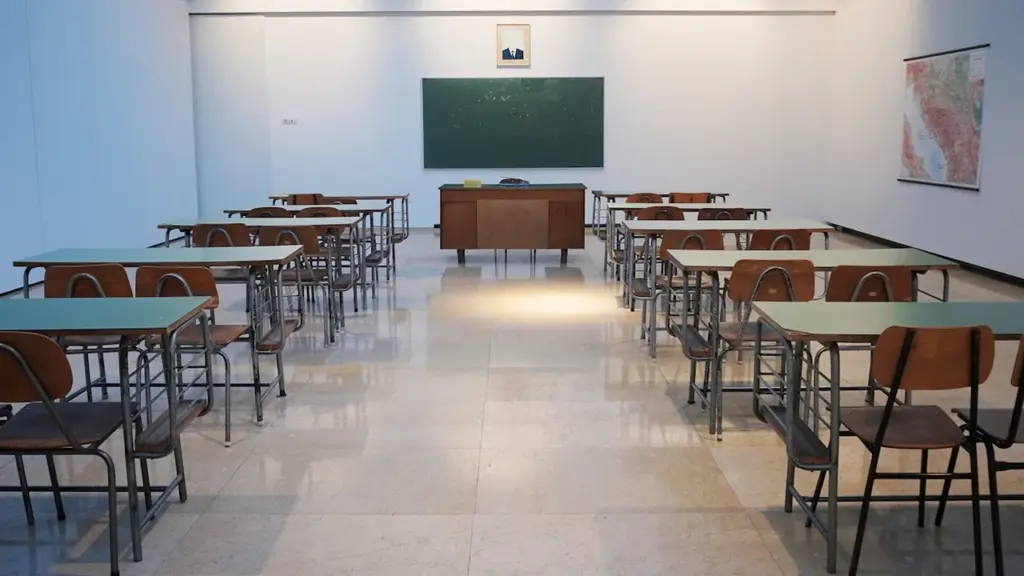 Empty classroom with rows of wooden desks and a green chalkboard in front.