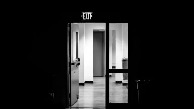 An illuminated exit sign above an open door in a dark hallway.