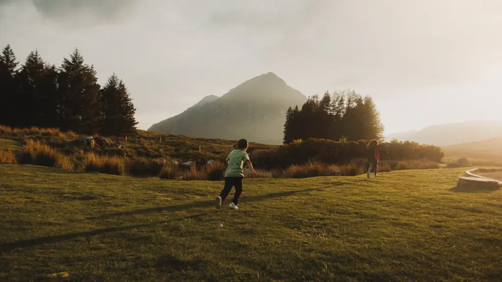 A child running through a vast green Scottish landscape with mountains in the background.