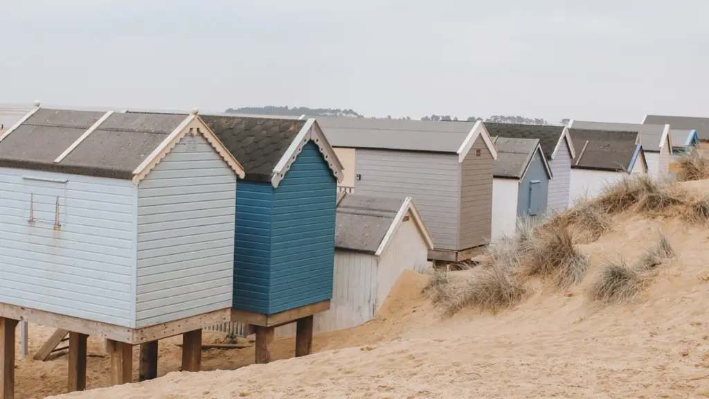 Colorful wooden beach huts on sandy dunes at a British seaside location.