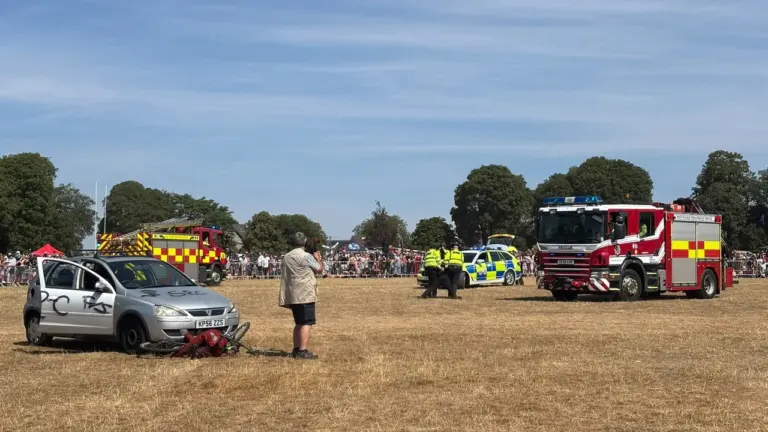Emergency vehicles and responders perform a public rescue demonstration on a dry grass field.