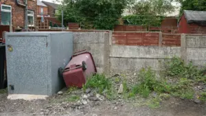A red council wheelie bin beside a storage unit in a British garden.