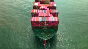An aerial view of a large container ship moving through calm green ocean waters.