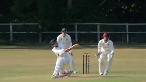 Two cricket players in white uniforms on a grass field during a sunny match.