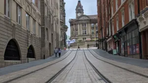 Tramlines leading through Birmingham city centre towards a historic brick building clock tower.