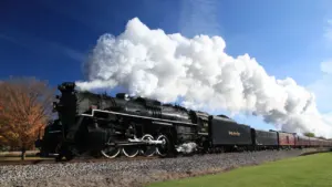 Heritage steam locomotive departing Haworth station under a historic stone railway bridge