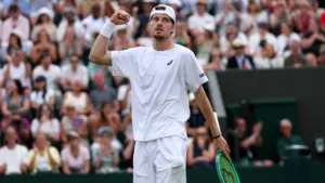 A tennis player in white athletic gear celebrates with a clenched fist on court.