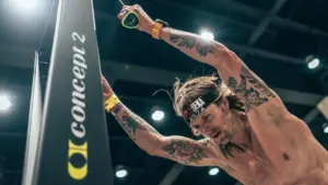 A tattooed man with a headband uses a Concept2 SkiErg exercise machine intensely.