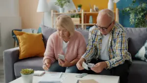 An elderly couple sitting on a sofa reviewing household financial documents together at home.