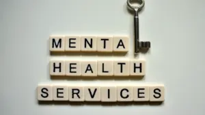 Scrabble tiles spelling Mental Health Services next to a silver key on white.