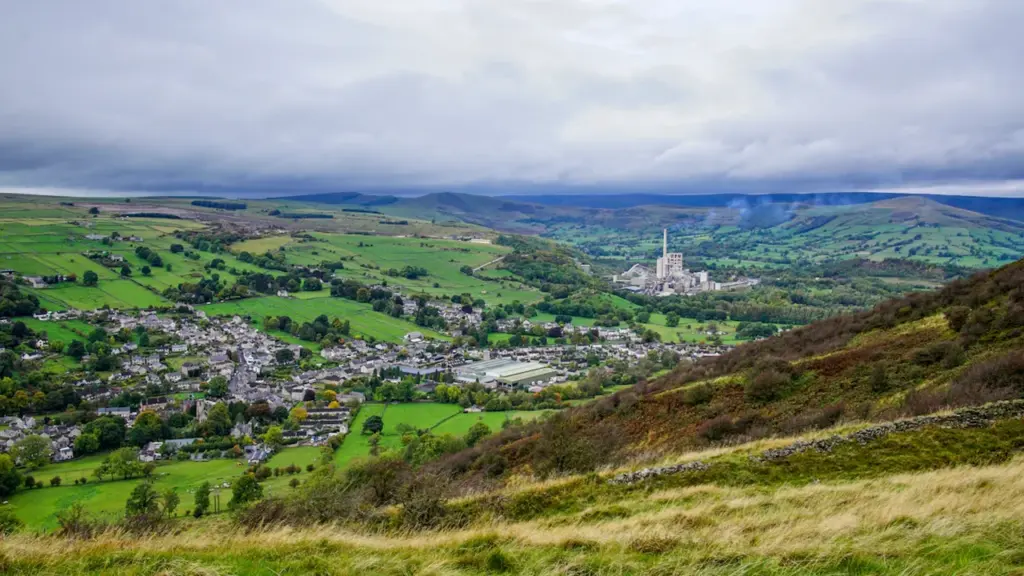 Panoramic view of a green valley town in the Peak District under clouds.