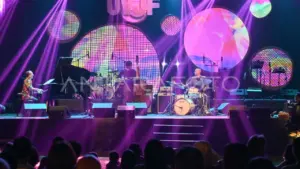 Live band performance under bright purple lights and abstract screen backdrop.