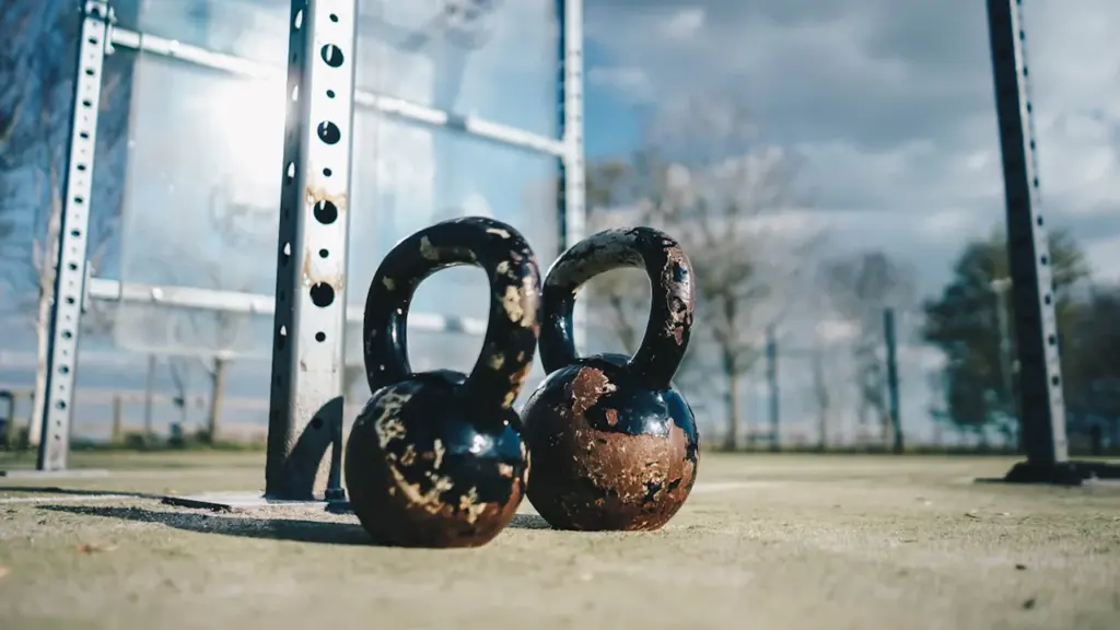 Two weathered kettlebells sitting on an outdoor gym ground in the UK.