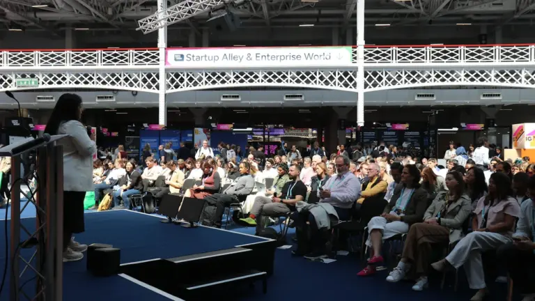 A speaker addressing a large audience at a professional indoor technology business conference event.