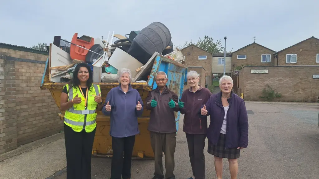 Five people stand giving thumbs up in front of a dumpster filled with trash.