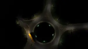 An aerial drone view of a yellow school bus navigating a dark roundabout at night.